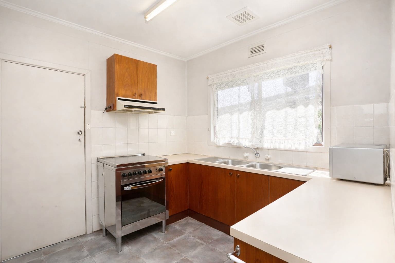 An original kitchen with timber cabinets, a laminate benchtop, a freestanding oven and a double sink under a window.