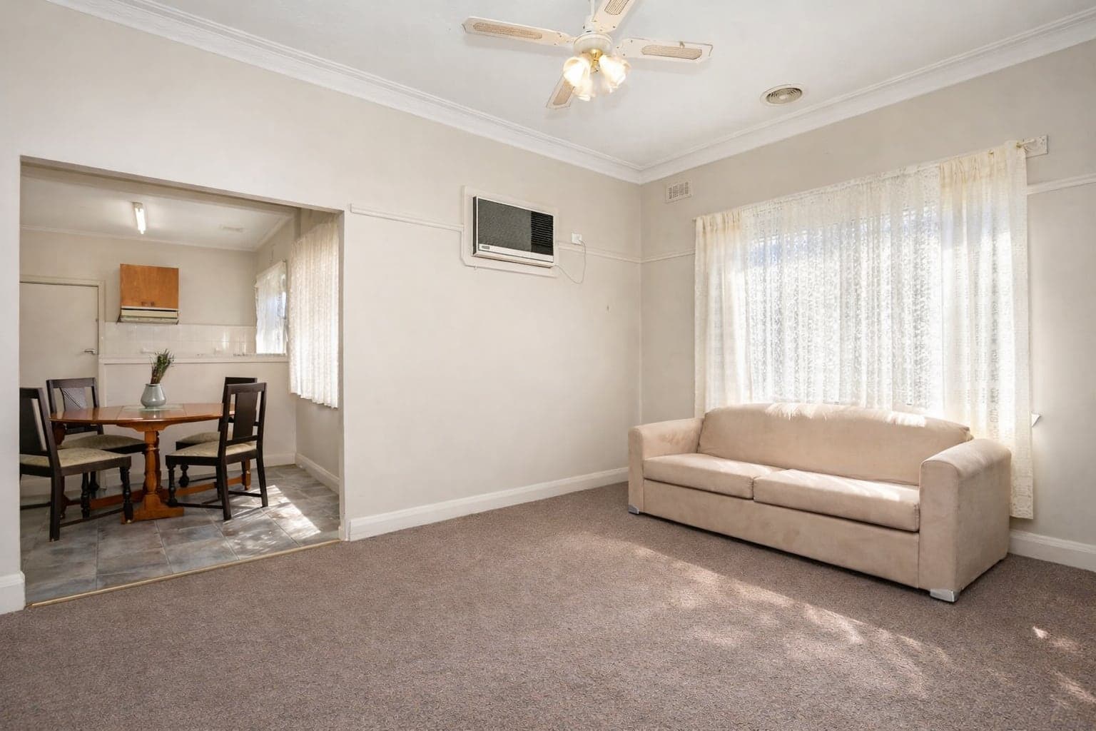 A carpeted living room with a sofa, ceiling fan and a wide opening through to the dining area.