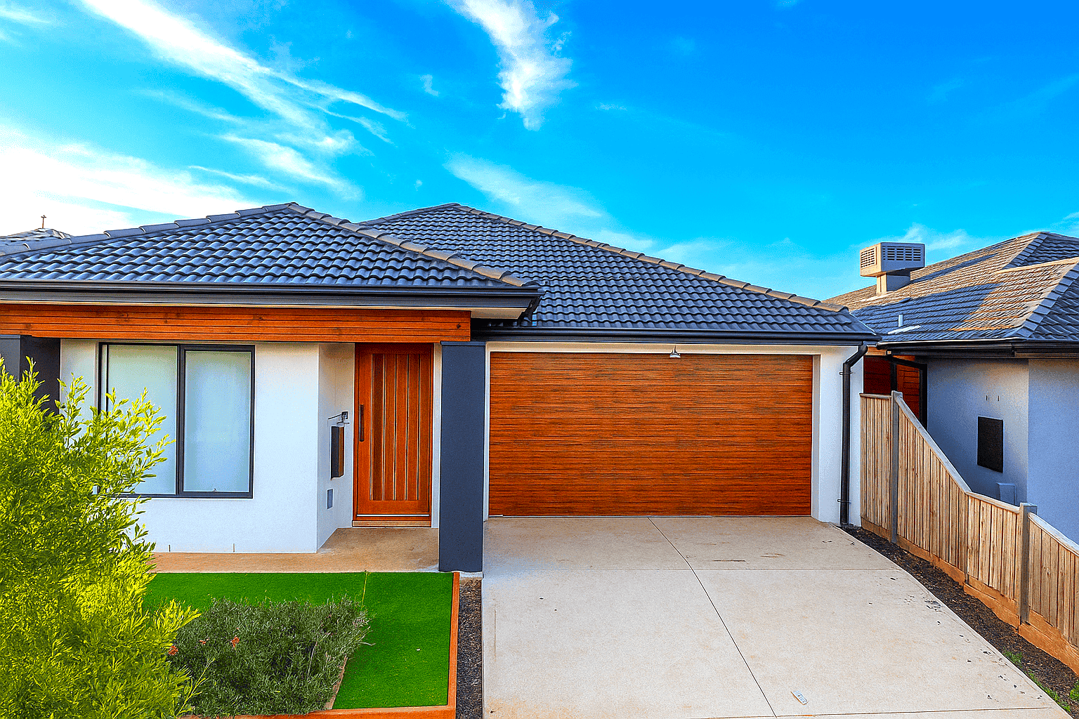 The front of the Deanside home: a single-storey house with a timber front door, a wide timber garage door and a flat concrete driveway.