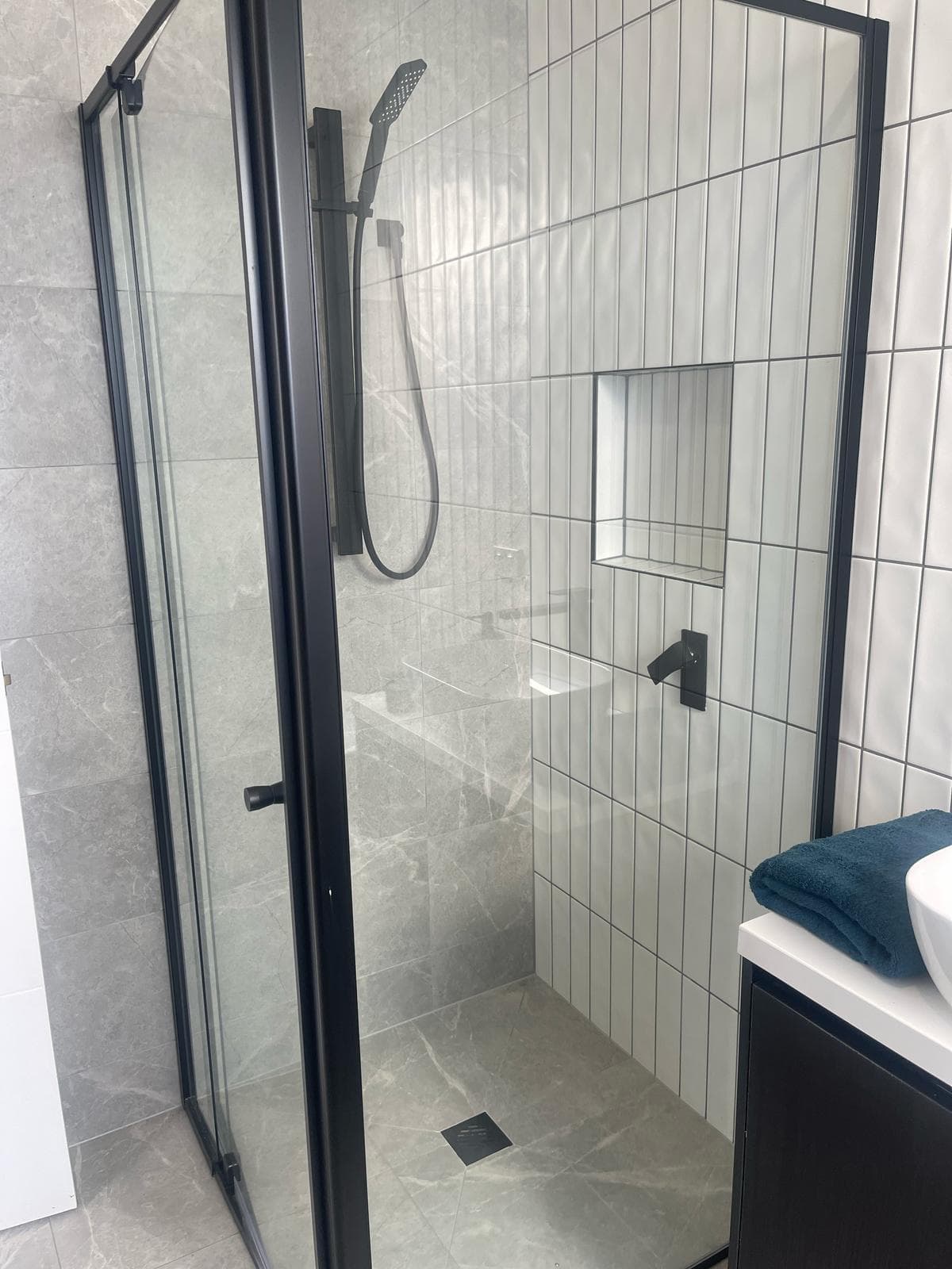 A tiled shower with a glass screen and a handheld shower head on an adjustable rail.